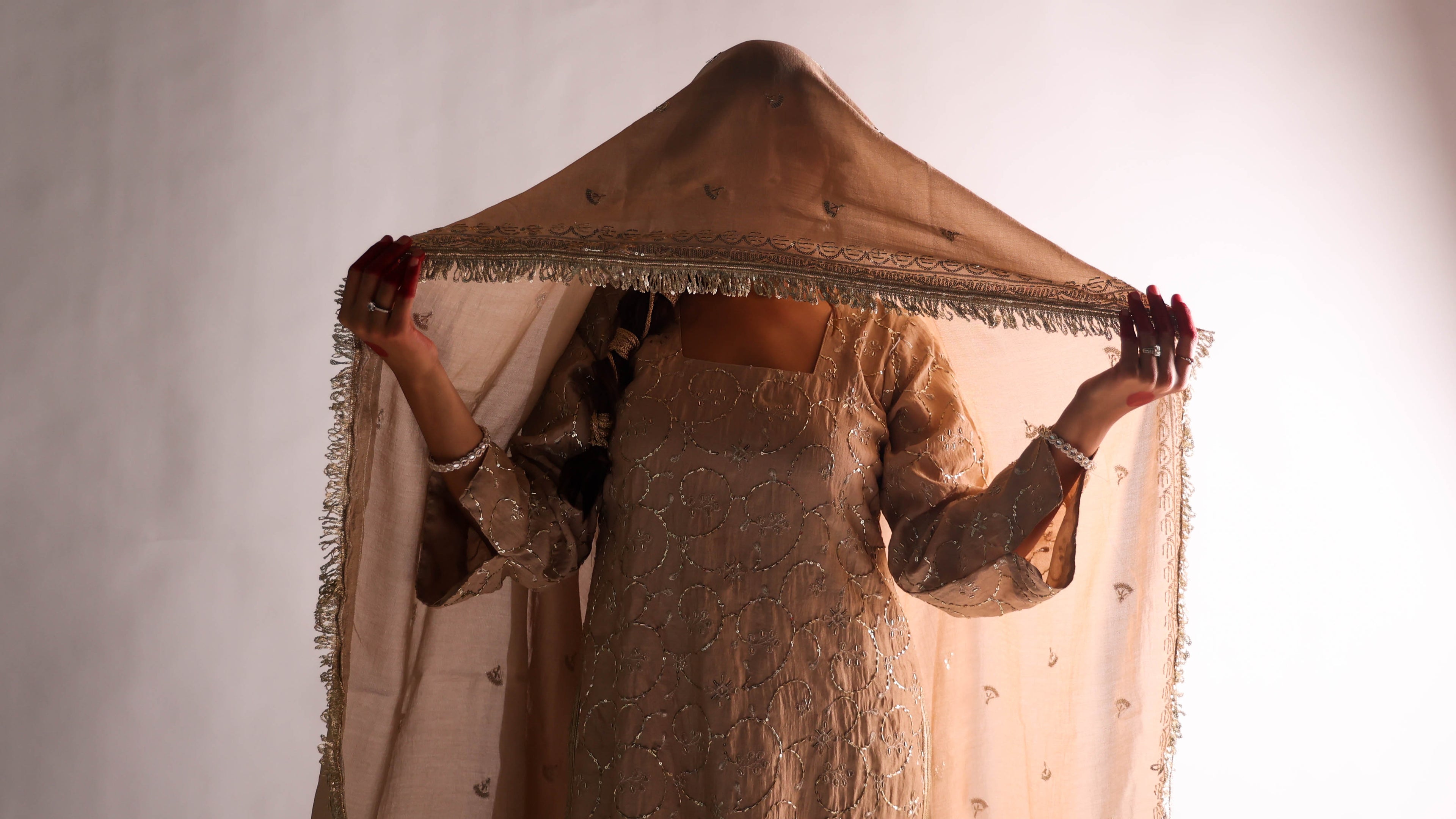 Person holding a decorative canopy over their head against a plain background
